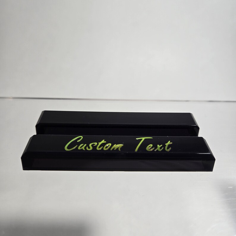 Puede incluir: Dos organizadores de escritorio rectangulares negros con bordes biselados. El organizador frontal tiene las palabras "Custom Text" en una fuente verde brillante, escrita a mano. Los organizadores est&aacute;n sobre una superficie reflectante.