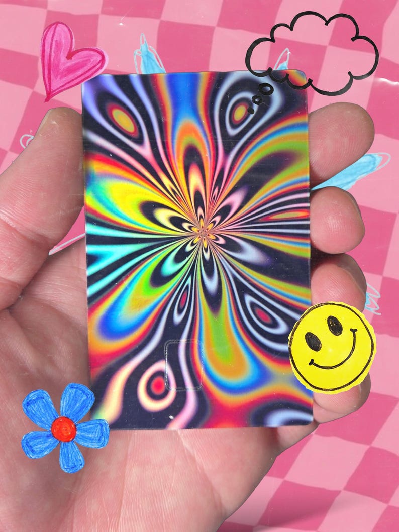 Pu&ograve; includere: Una carta rettangolare con un vivace design psichedelico nei toni del blu, giallo, verde e rosso &egrave; tenuta in mano. La carta presenta un motivo a spirale a forma di fiore. Un adesivo giallo con la faccina sorridente e altri scarabocchi circondano la carta.