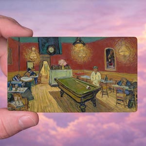 May include: A rectangular painting depicting Van Gogh's "The Night Cafe" with a green pool table, figures at tables, and a clock on the wall. The artwork is held against a backdrop of a pink and purple sky.