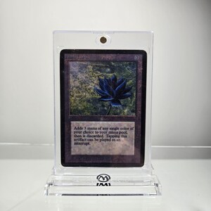 May include: A black Magic: The Gathering card with a black lotus flower on a green background. The card text reads "Blank Lotus" and "Adds 3 mana of any single color of your choice to your mana pool, then is discarded. Tapping this artifact can be played as an interrupt."