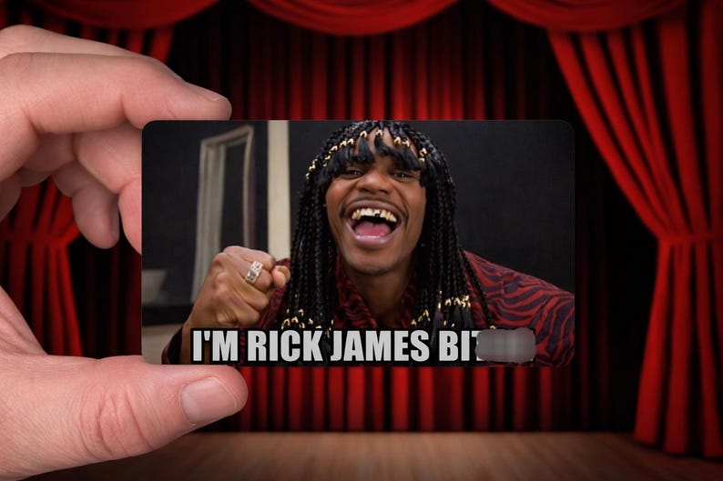 May include: A rectangular card featuring a smiling person with long braids and a red patterned shirt. The card has the text "I'M RICK JAMES BI". The card is held in front of a red curtain.