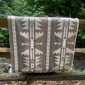 May include: A brown and white woven throw blanket with a geometric pattern of arrows and triangles. The blanket is fringed on the bottom edge.