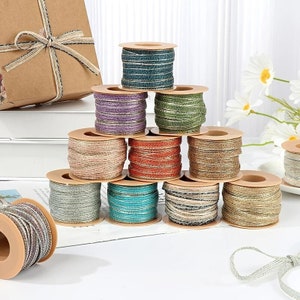 May include: A collection of ten spools of twine in various colours, including teal, gold, pink, orange, and green. The spools are arranged in a pyramid shape on a white surface.