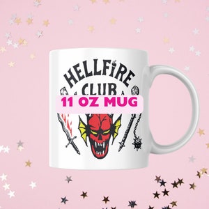 May include: White ceramic mug with a black and red illustration of a demon head with a crown and the text "Hellfire Club 11 oz Mug".
