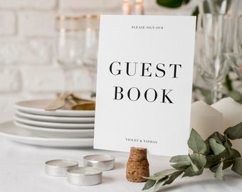 Puede incluir: Tarjeta blanca con texto negro que dice "Por favor, firme nuestro libro de visitas Violet & Nathan" en una mesa con velas, vasos y vegetación.