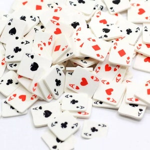 May include: A pile of white playing cards with red and black suits. The cards are all aces and are scattered on a white surface.