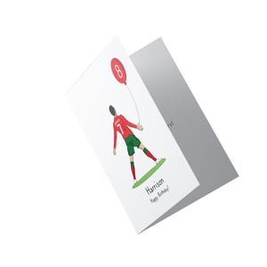 May include: A white card with a red and green illustration of a soccer player holding a red balloon with the number 8 on it. The text "Harrison Happy Birthday!" is printed on the card.
