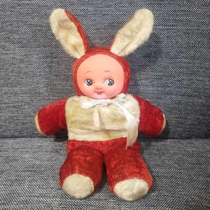 May include: A plush bunny rabbit toy with a red and white outfit and a smiling face. The toy has large, black eyes and a white bow tie.