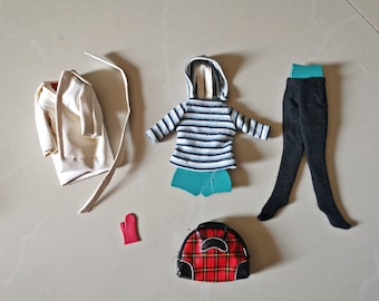 May include: A collection of doll clothing including a cream-coloured trench coat with a belt, a blue and white striped hooded jumper, a pair of black leggings with a teal waistband, a single red mitten, and a red and black plaid handbag.