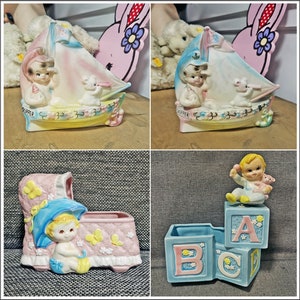 May include: A collection of vintage ceramic baby-themed planters. One planter is a boat with a baby and a mouse, another is a baby in a crib, and the last is a baby on ABC blocks. The planters are painted in pastel colors.