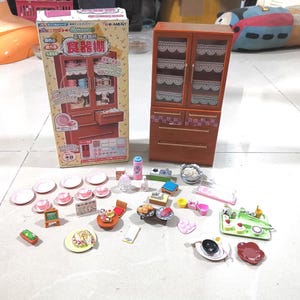 Könnte beinhalten: Ein Miniatur-Küchenset mit einem Holzschrank, Geschirr und Lebensmitteln. Das Set enthält Teller, Tassen, einen Tisch, Stühle und verschiedene Lebensmittelminiaturen. Auf der Box steht "ぷちお台所 食器棚" auf Japanisch.