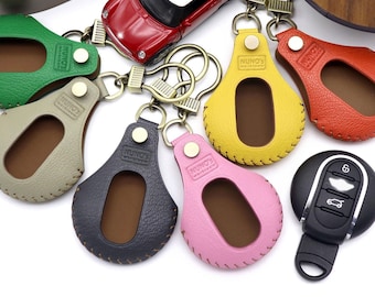 May include: A set of seven keychains with different colored leather covers. Each keychain has a small window to display a car key. The keychains are arranged in a circle around a black car key with a silver button. The keychains are labeled with the brand "NUNO'S".