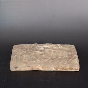May include: A rectangular stone slab with a raised, detailed carving of a dragon. The carving is in a light brown color and the stone has a rough texture.