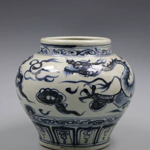 May include: A white porcelain jar with a blue and white dragon design. The jar has a round body and a flared lip. The dragon is depicted in flight, with its claws outstretched. The jar is decorated with clouds and other decorative elements.