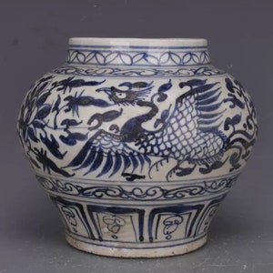 May include: A white ceramic jar with a blue and white design of a phoenix and floral patterns. The jar has a round body and a wide mouth.