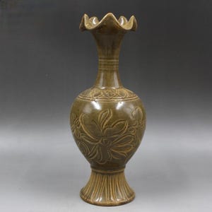 May include: A green ceramic vase with a scalloped rim and intricate floral carvings. The vase has a bulbous body and a flared base.