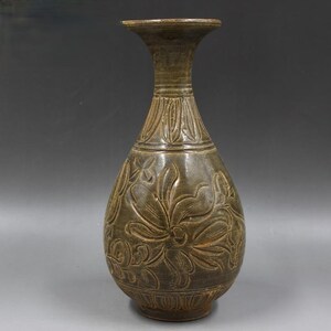 May include: A green ceramic vase with a wide mouth and a narrow neck. The vase is decorated with a carved floral design.