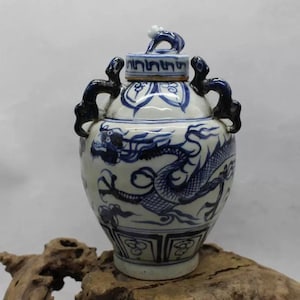 May include: A small, blue and white porcelain vase with a dragon design and a lid. The vase has two handles and a round body.