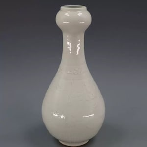 May include: White porcelain vase with a bulbous body and a narrow neck. The vase is decorated with an embossed floral design.
