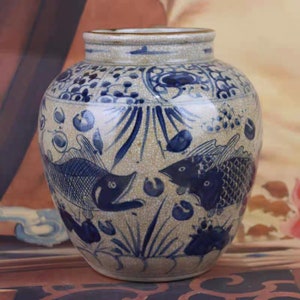 Può includere: Un vaso di ceramica bianca con disegni di pesci blu e bianchi. Il vaso ha un corpo rotondo e una bocca larga.