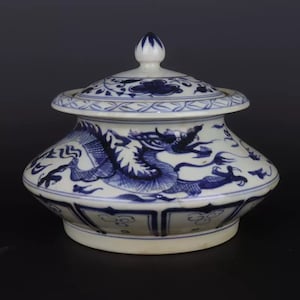 May include: A white and blue ceramic jar with a lid. The jar features a detailed blue dragon design on the body and floral patterns on the lid. The jar has a bulbous shape with a decorative finial on top.