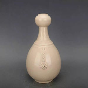 Könnte beinhalten: Eine weiße Keramikvase mit einem bauchigen Körper und einem schmalen Hals. Die Vase hat ein erhabenes Blumenmuster und eine Reihe kleiner Punkte um den Hals.