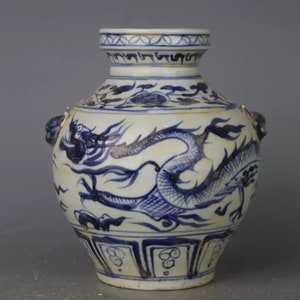 May include: A white porcelain vase with blue and white dragon design. The vase has two handles in the shape of dragon heads. The vase has a round body and a narrow neck.