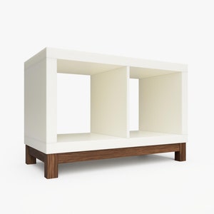 May include: White bookshelf with two open shelves and a brown wood base. The bookshelf is made of wood and has a modern design.