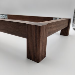 May include: A wooden frame with a dark brown finish. The frame is made of thick, sturdy wood and has a rectangular shape. The frame is designed to be used as a base for a variety of objects.