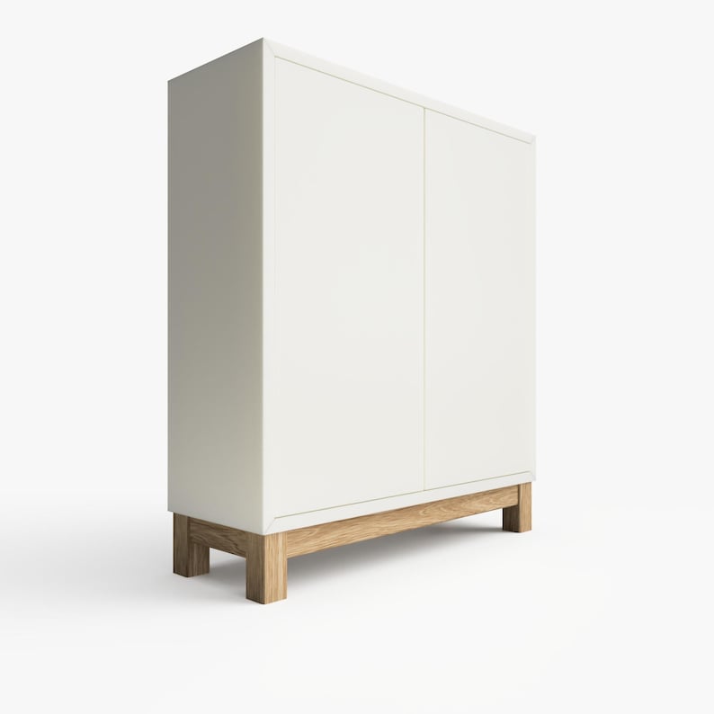May include: A white cabinet with two doors and wooden legs. The cabinet has a simple design and is made of a smooth, white material.