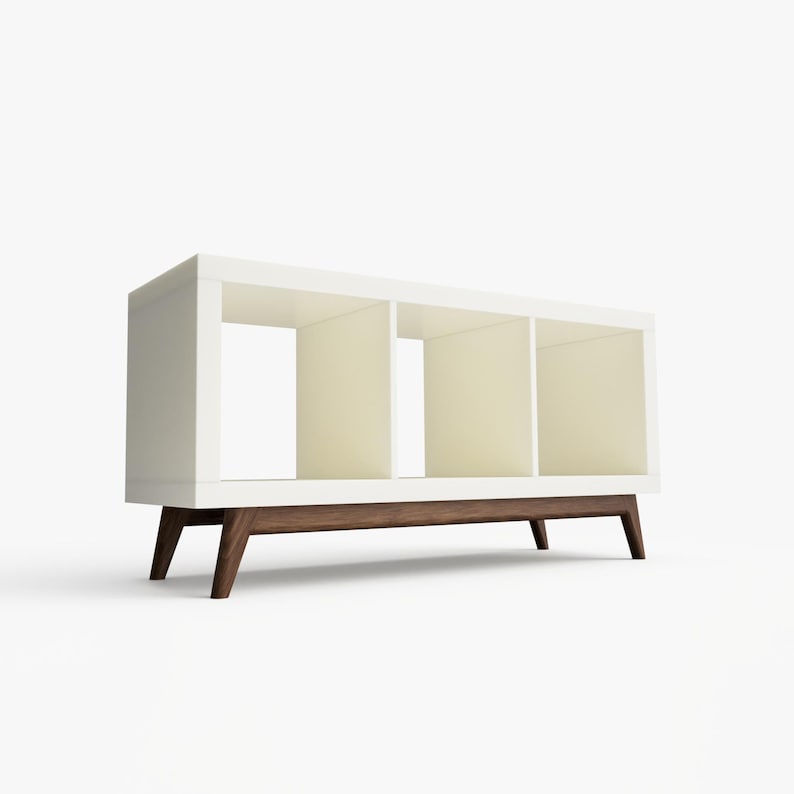 May include: White bookshelf with three open shelves and a dark wood base with four legs.