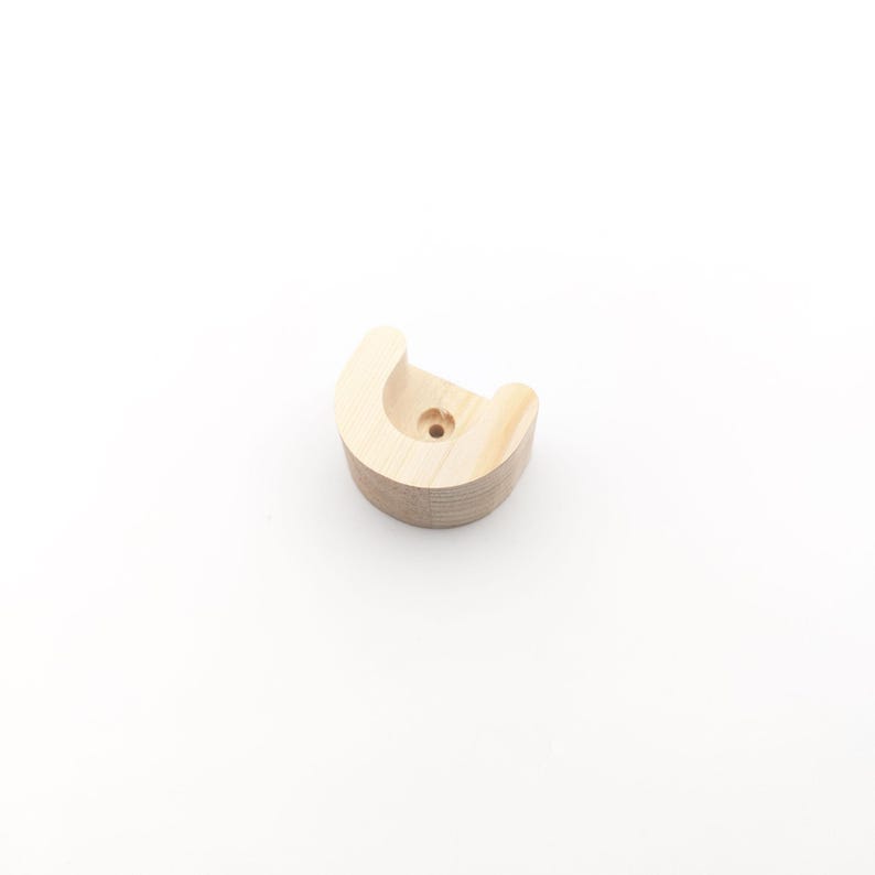 May include: A light-coloured, unfinished wooden bracket with a curved design. The bracket has a rounded top with a small hole in the centre. The item is made of layered wood and is designed to be mounted on a wall.