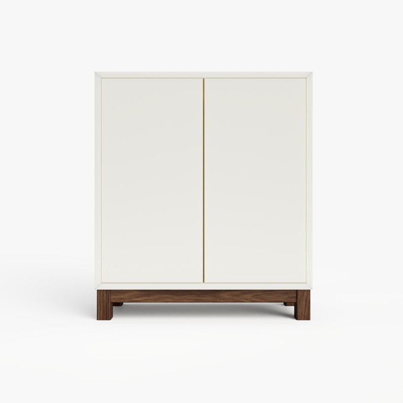 May include: White cabinet with two doors and a wooden base. The cabinet has a simple design and is made of a smooth, white material.