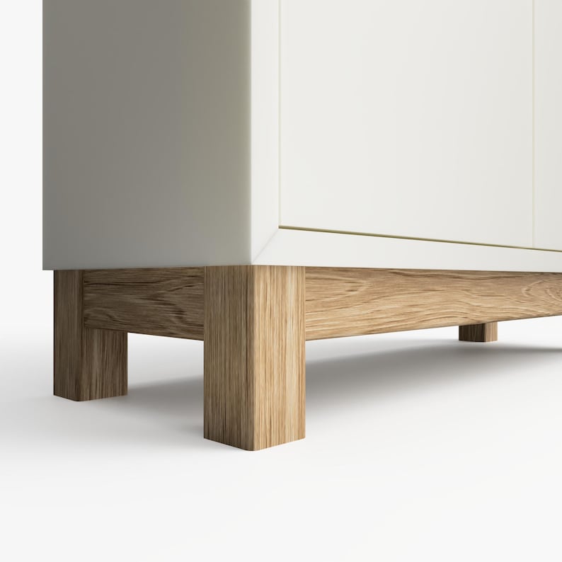 May include: White cabinet with wooden legs. The cabinet has a simple design and is made of a light-colored wood.