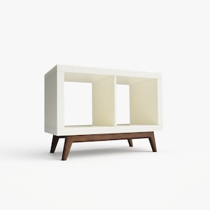 May include: White bookshelf with two open shelves and a brown wood base. The bookshelf has a modern design with angled legs.