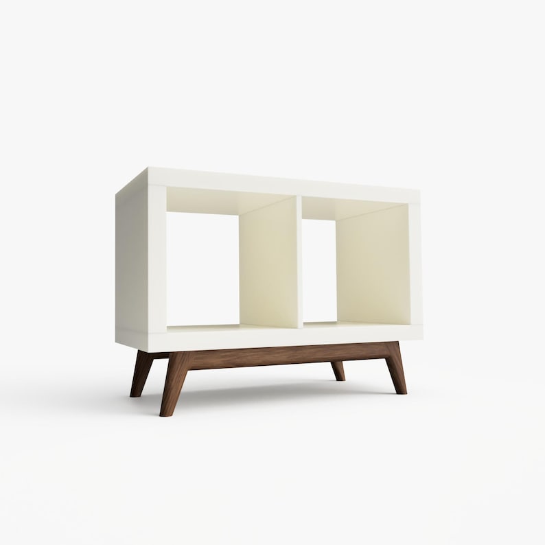 May include: White bookshelf with two open shelves and a brown wood base. The bookshelf has a modern design with angled legs.