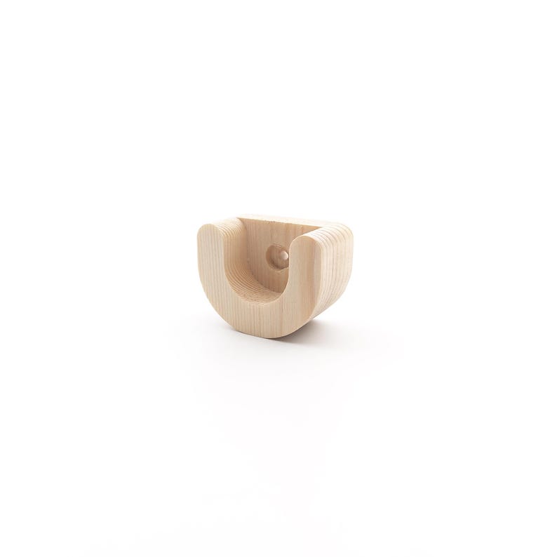 May include: A light-coloured, wooden U-shaped bracket with a rounded design. The bracket has a hole in the centre and is made of layered wood. The object is likely a wall-mounted support for a curtain rail or similar item.