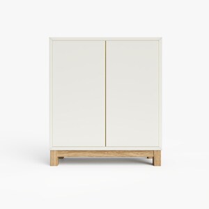 May include: White cabinet with two doors and a wood base. The cabinet has a simple design and is made of a light-colored wood.