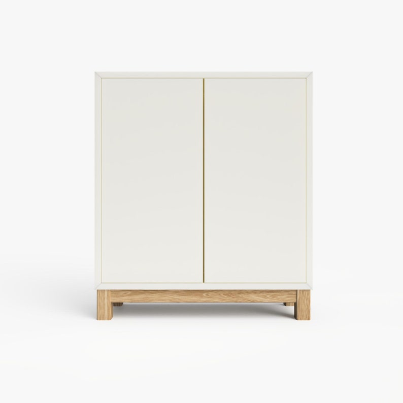 May include: White cabinet with two doors and a wood base. The cabinet has a simple design and is made of a light-colored wood.