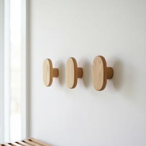 Puede incluir: Tres perchas de pared de madera con diseño ovalado están montadas en una pared blanca. Las perchas son de madera de color claro y tienen una estética sencilla y minimalista. Las perchas están espaciadas uniformemente y ofrecen una solución de almacenamiento funcional y decorativa.