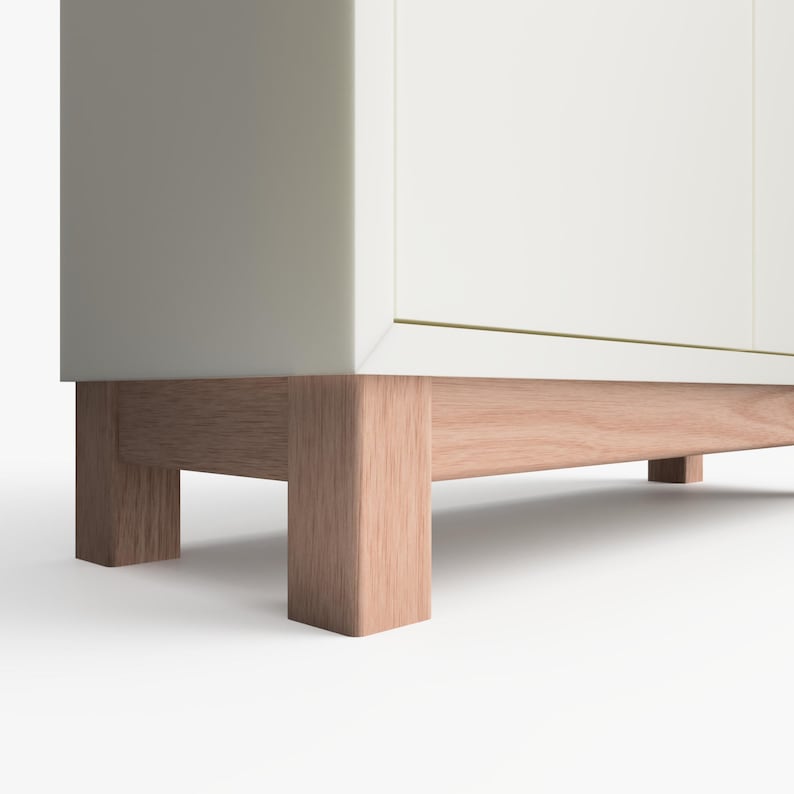 May include: White cabinet with wooden legs. The cabinet has a simple design and is made of a light-colored wood.