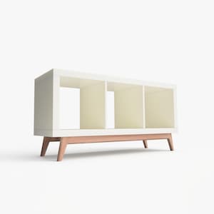 May include: White bookshelf with three open shelves and a wooden base. The bookshelf has a modern design with angled legs.