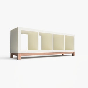May include: White bookshelf with four open shelves and a wooden base. The bookshelf is made of wood and has a modern design.