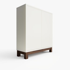 May include: A white cabinet with two doors and a wooden base. The cabinet has a simple design and is made of a smooth, white material.