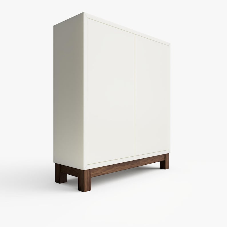 May include: A white cabinet with two doors and a wooden base. The cabinet has a simple design and is made of a smooth, white material.