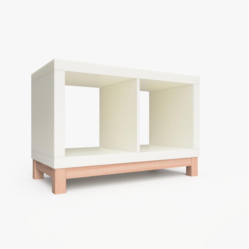 May include: White shelf unit with two open compartments and a natural wood base. The shelf unit is made of wood and has a modern design.