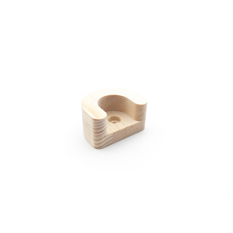 May include: A light-coloured wooden bracket with a curved top and a cylindrical hole. The bracket is made of layered wood and has a smooth, natural finish. The design is simple and modern, suitable for various home decor styles.