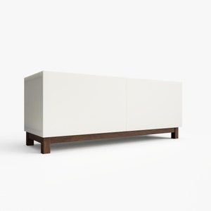 May include: White media console with two doors and a dark wood base. The console is sitting on a white surface.