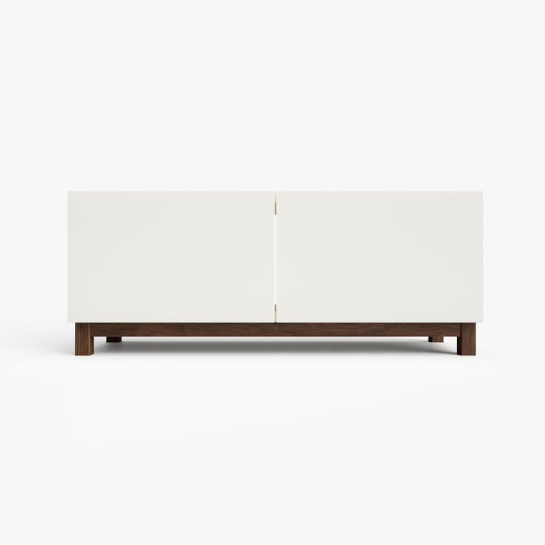 May include: A white media console with two doors and a wood base. The console has a modern design and is perfect for storing electronics and other media.