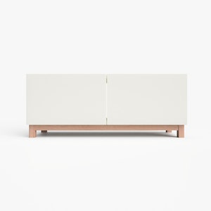 May include: White media console with two doors and a wood base. The console has a simple, modern design.
